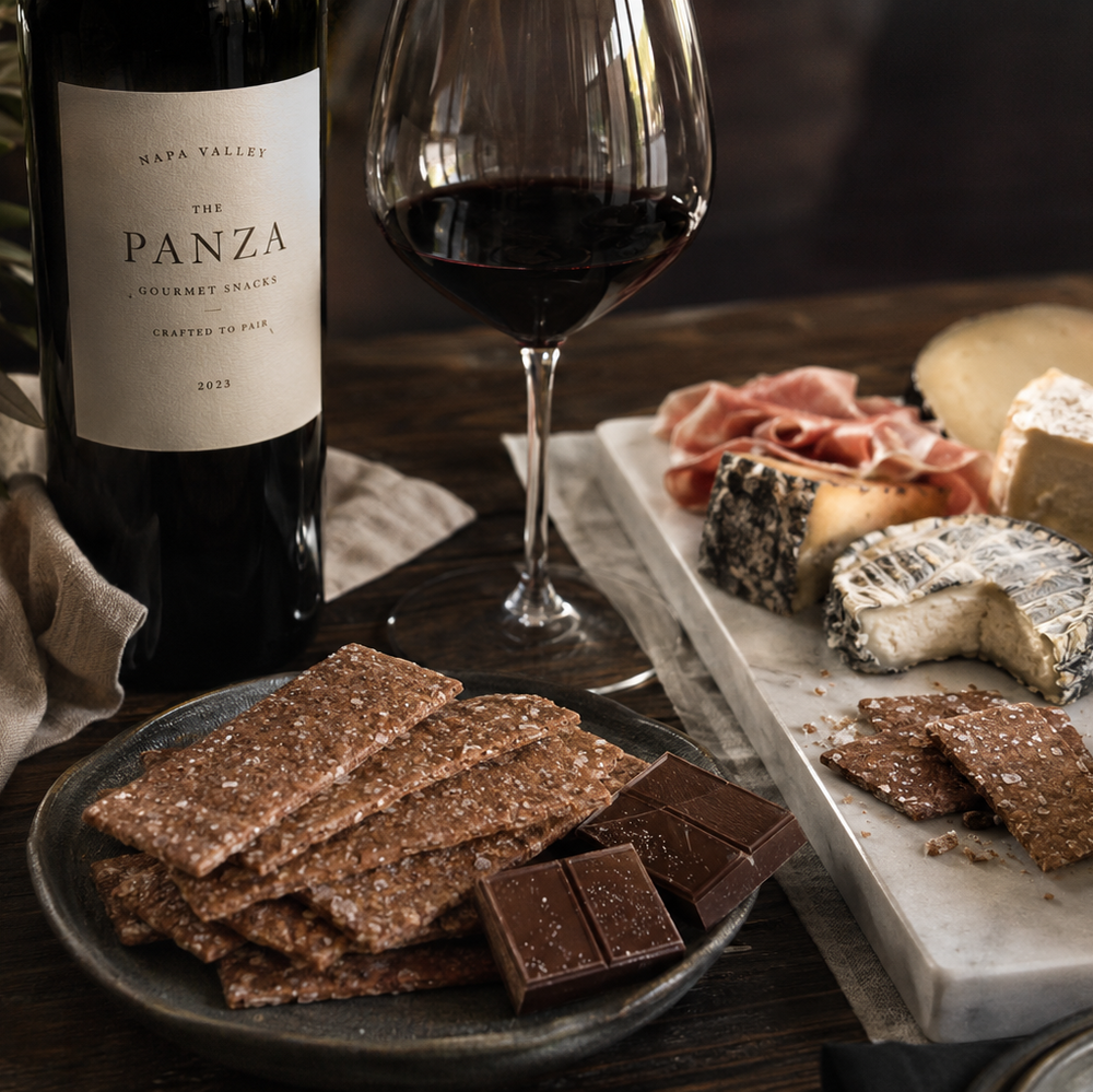 Wine bottle, glass, and charcuterie board with Panza wine on a wooden table and The Panza premium cookies on plate.
